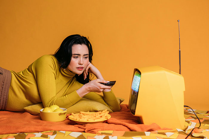 Woman watching vintage TV while surrounded by retro decor, reflecting 1980s fashion culture